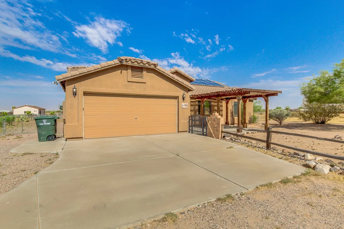 The image highlights a spacious front yard with a welcoming porch, garage, thoughtfully landscaped surroundings, and visible solar panels. The atmosphere is peaceful and inviting, perfect for enjoying quiet mornings or watching sunsets.