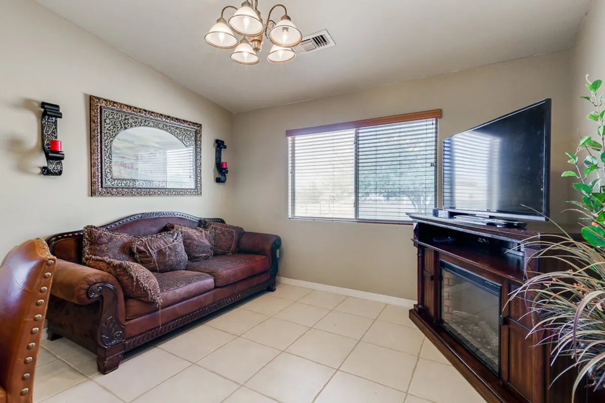 A cozy living room centered around a plush leather couch, with a decorative mirror above, a large television for movie nights, and warm sconces providing ambient lighting. The space feels intimate and inviting, perfect for gathering with family or friends.