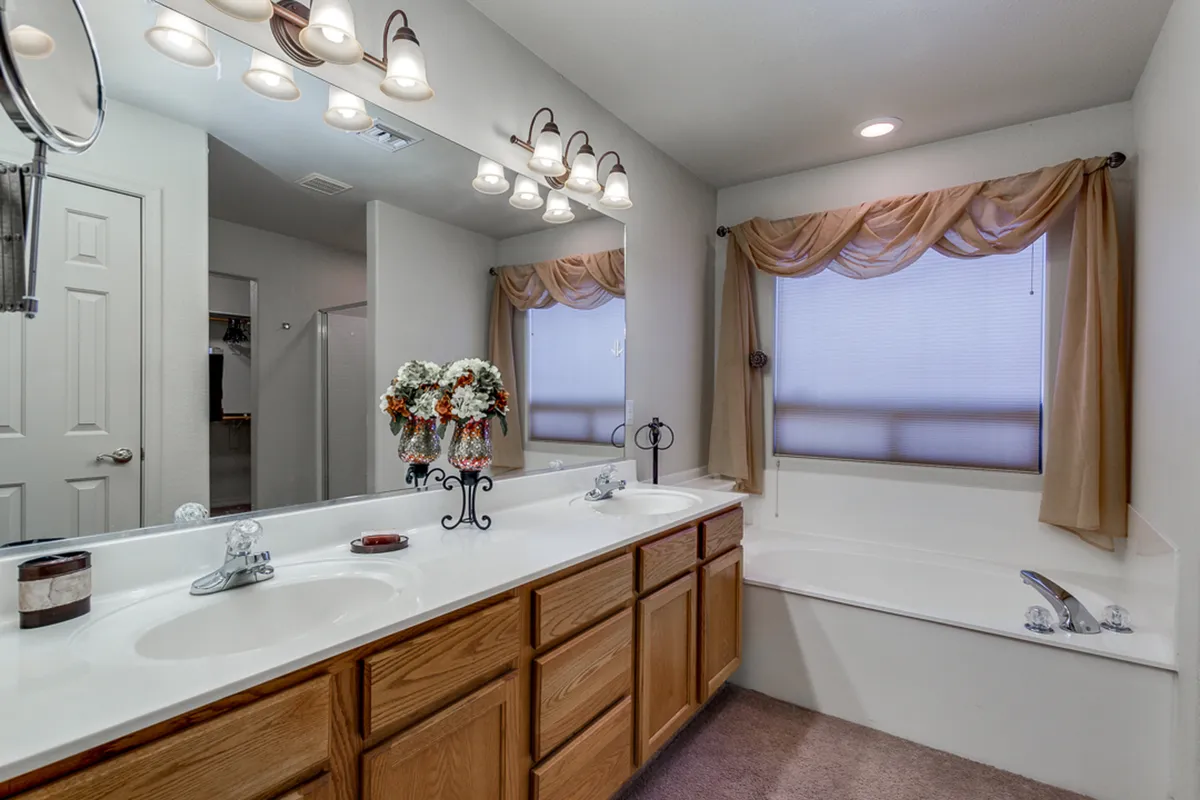 A calm and serene bathroom featuring a double vanity sink, a decorative floral arrangement, a bathtub, and elegant lighting. The room exudes a spa-like feel, ideal for self-care routines and unwinding at the end of the day.