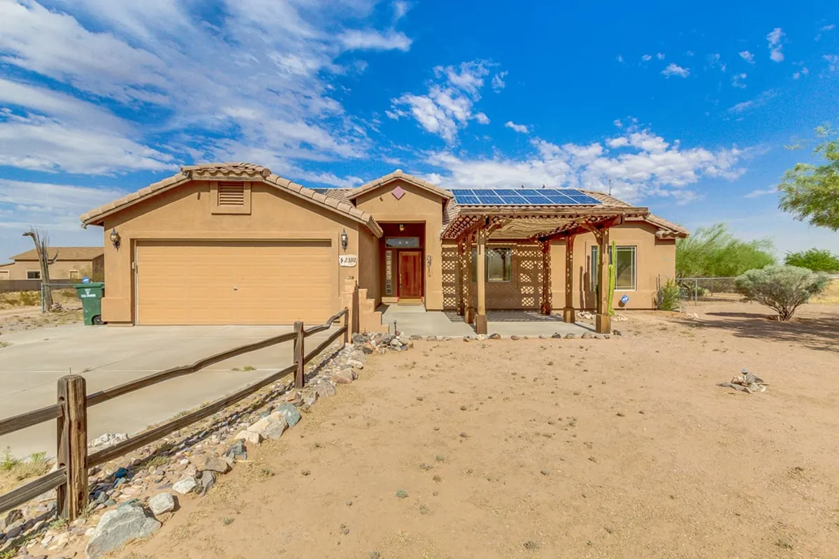 The welcoming front porch showcases lattice work, desert landscaping, solar panels, and a garage door. The space is serene and ideal for relaxing, watching sunsets, or gathering outside, with practical features for family needs.