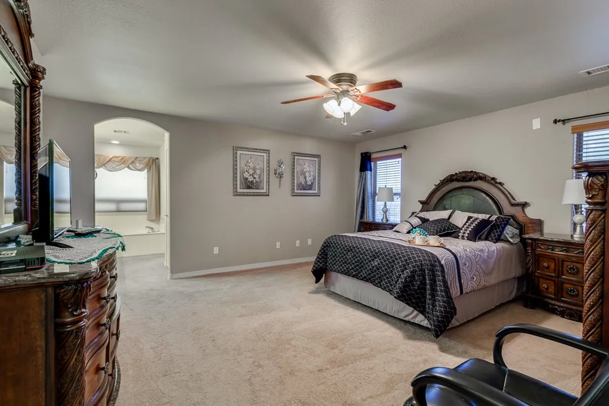 A relaxed bedroom with a bed adorned with decorative pillows, a wooden dresser, and framed artwork on the walls. The soft lighting and cozy atmosphere offer a glimpse into a peaceful space ideal for morning coffee or evening reading.