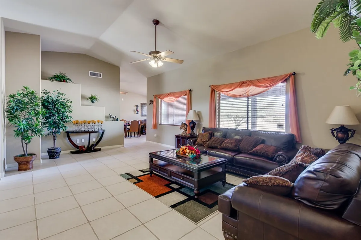 A comfortable living space featuring a leather sofa, a coffee table with decorative accents, and large windows draped with curtains that reveal glimpses of the surrounding landscape. The inviting setup is perfect for gatherings, reading, or simply soaking in the views.