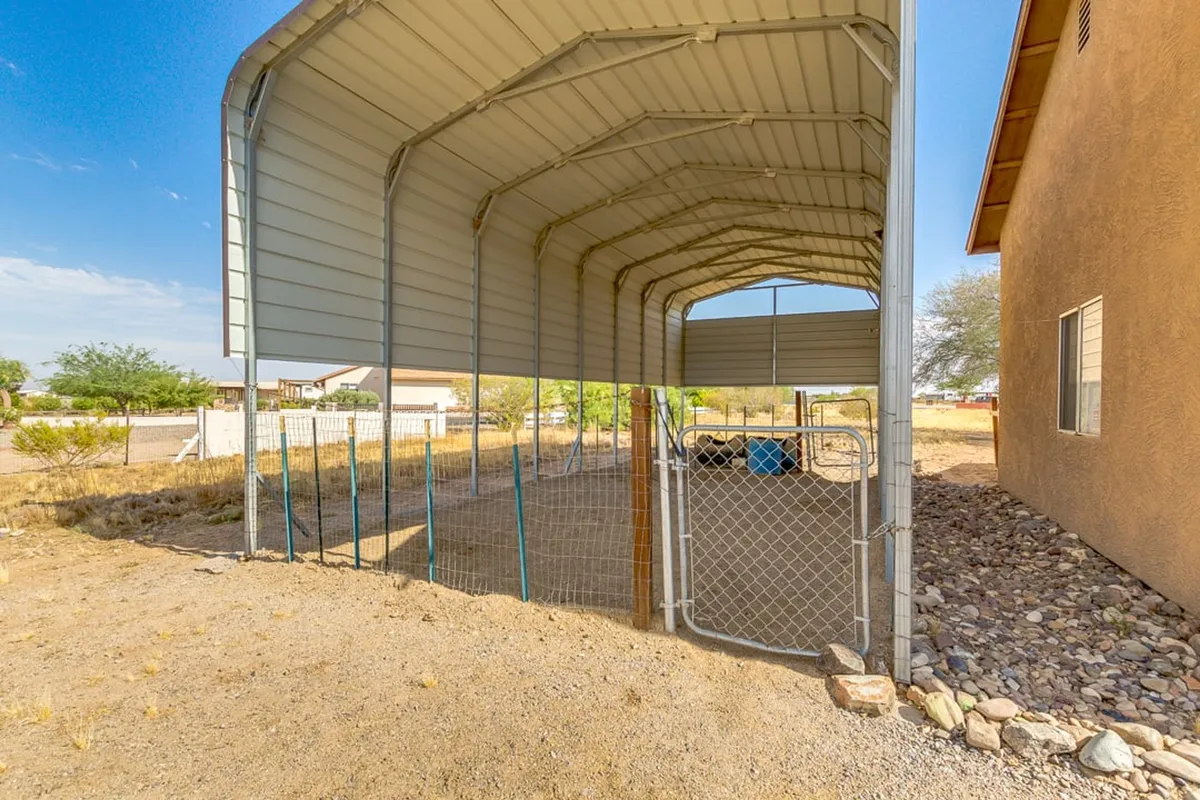 This image depicts a practical metal structure with a fenced area and dirt ground, set against the backdrop of the surrounding landscape. The utilitarian design and ample open space suggest areas suitable for horses, trailers, and equipment associated with equestrian activities.