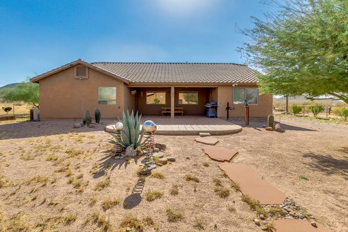 A welcoming patio area is surrounded by succulent plants and pathways, with the house nearby and the expansive sky overhead. The arrangement invites gatherings, outdoor dining, and sunset watching, with clear sightlines to the open land beyond.