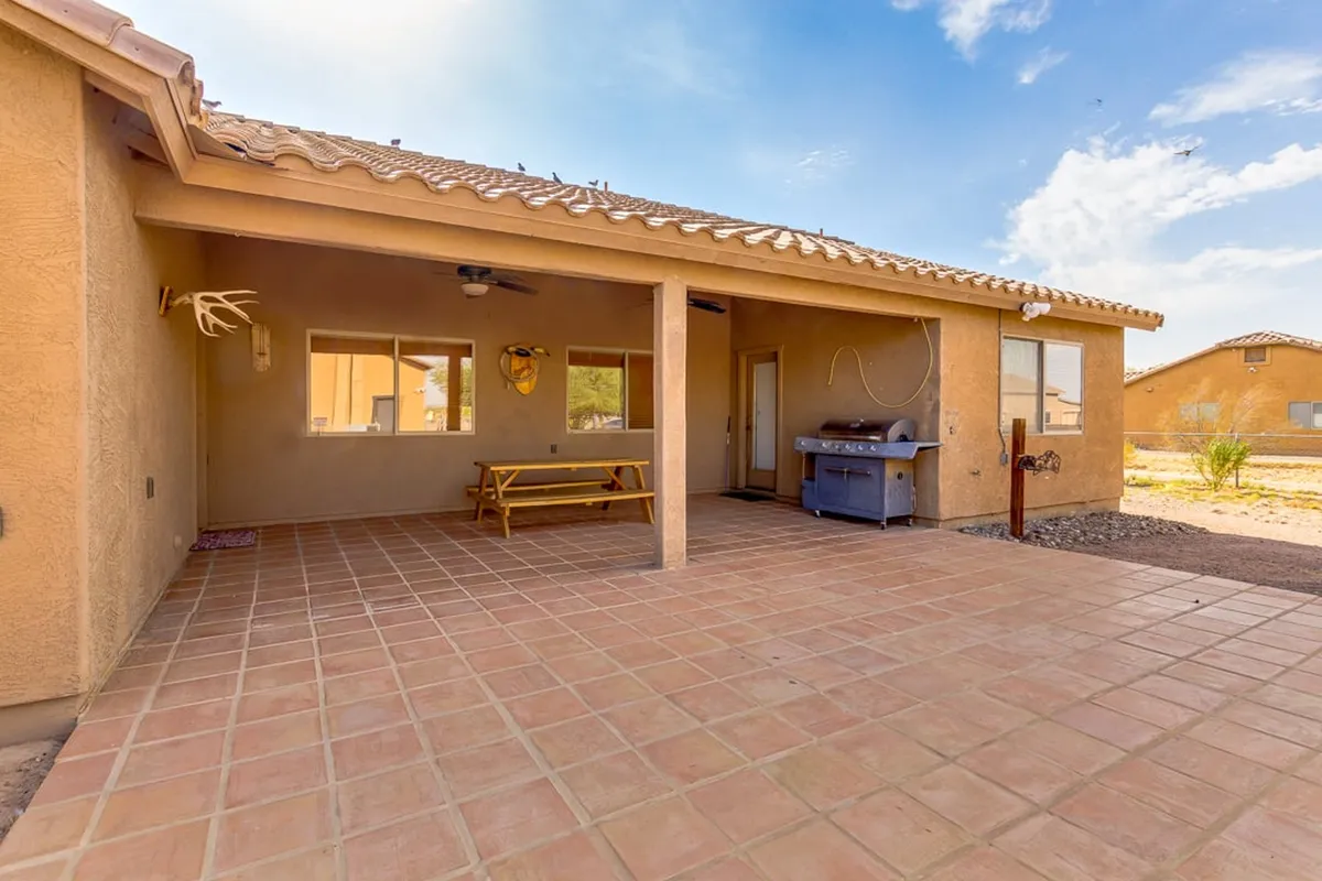 This exterior shot features comfortable patio seating, a grill, and large windows looking into the home. The setting is casual and welcoming, ideal for outdoor dining, relaxing with friends, or enjoying a peaceful Arizona evening.
