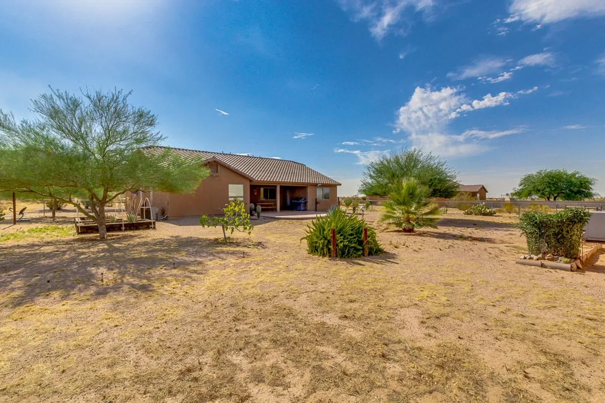 This exterior image features the home set against tranquil natural surroundings, with lush vegetation and a serene patio area visible. The view suggests expansive outdoor space and a clear vantage for watching sunsets or relaxing in the evening.